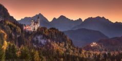 Alpenpanorama in Bayern mit den beleuchteten Königsschlössern Neuschwanstein und Hohenschwangau im Herbst zum Sonnenuntergang