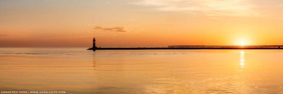 * Warnemünde Leuchtturm im Sonnenaufgang * Kleiner Leuchtturm im Sonnenaufgang an der Hafeneinfahrt zum Hafen in Warnemünde an der Ostsee.