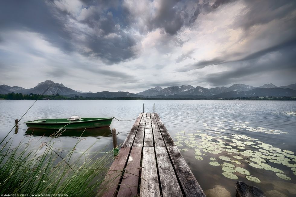 * Steg am See 2 * . Stimmungsvoller Hopfensee in den allgäuer Alpen. Dramatischer Himmel am See mit blühenden Seerosen und den Alpen im Hintergrund.