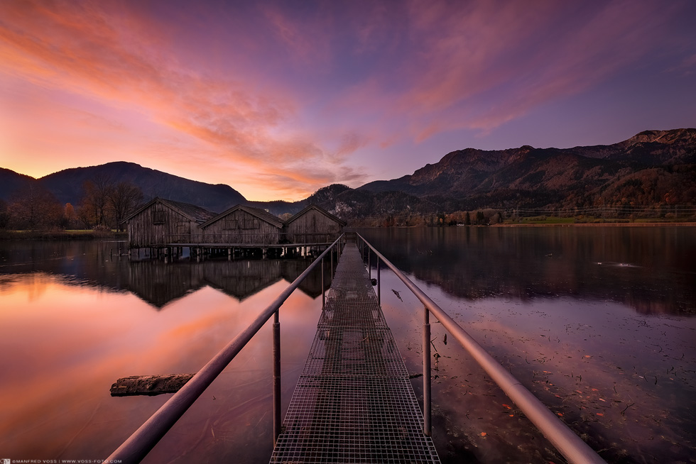 Landschaft mit Sonnenaufgang am Kochelsee in den Alpen in Bayern mit drei Bootshäusern