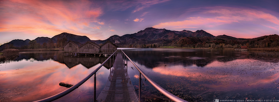 Panorama Landschaft mit Sonnenaufgang am Kochelsee in den Alpen in Bayern mit drei Bootshäusern