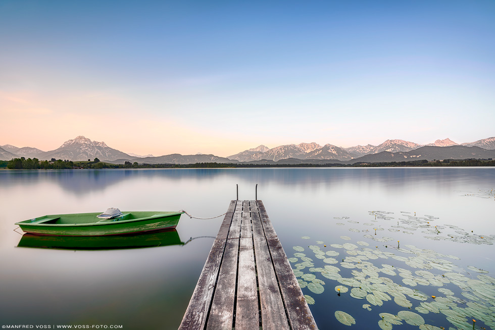 * Steg am See 3 * . Stimmungsvoller Hopfensee in den allgäuer Alpen. Dramatischer Himmel am See mit blühenden Seerosen und den Alpen im Hintergrund.
